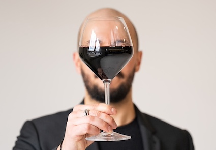 A glass of full-bodied red wine in front of the face of a WinesnVines founder, inspired by Magritte's style. Buy Italian Wine Online.